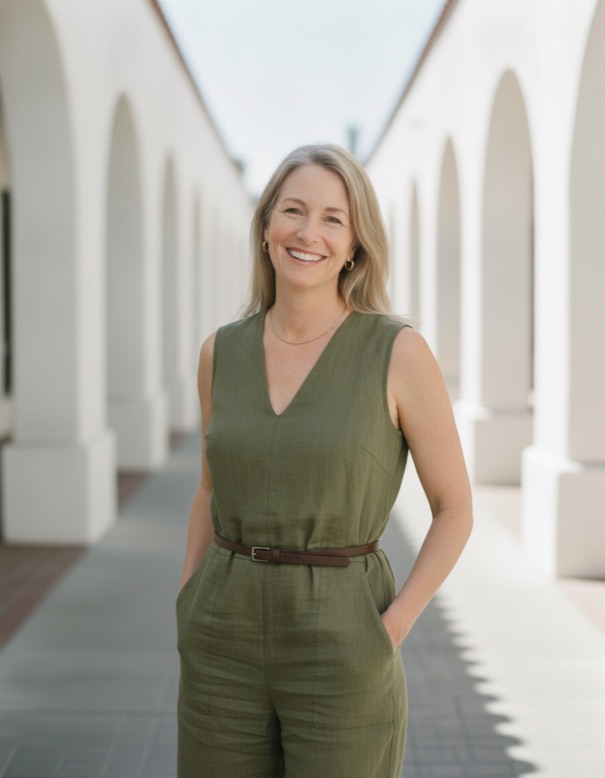Claire in an olive linen jumpsuit under white mission arches, smiling